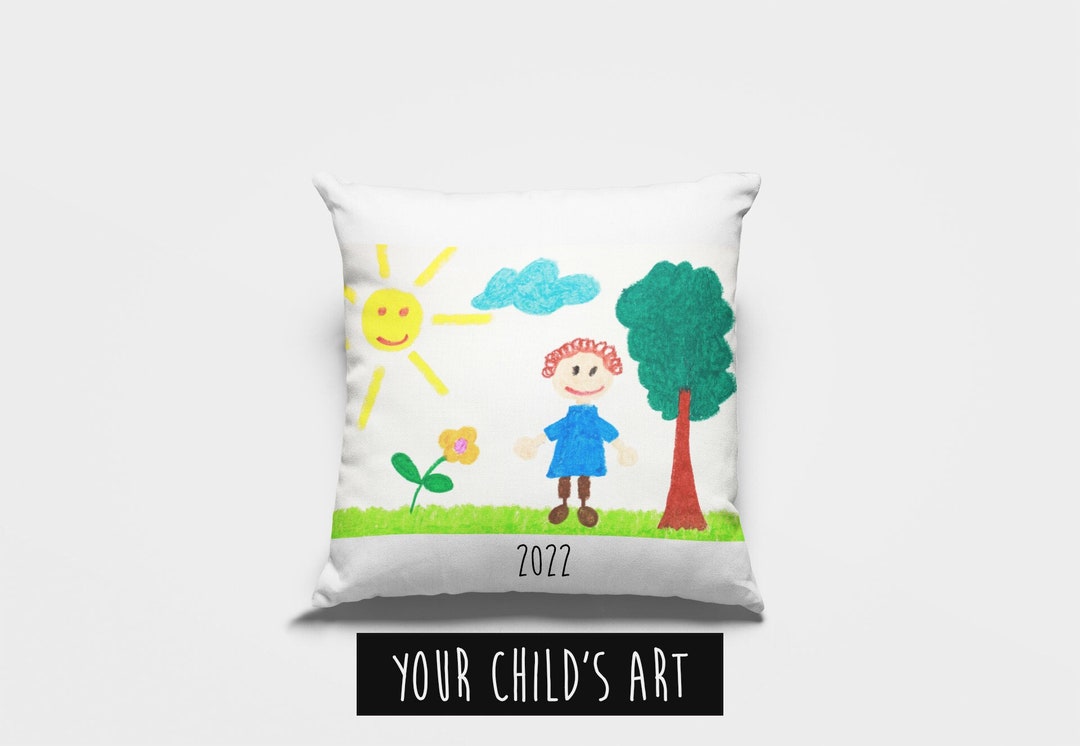 White throw pillow with child's crayon drawing of person, sun, cloud, flower and tree